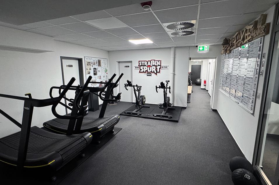 Fitnessraum mit zwei Laufbändern und Trainingsgeräten, Wänden in neutralen Farben und einem angrenzenden Wandboard.