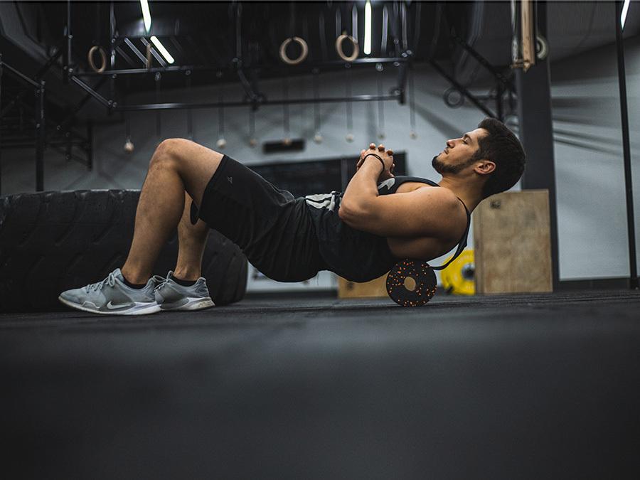 Mann in Sportkleidung verwendet eine Faszienrolle auf dem Boden im Fitnessstudio zur Muskelentspannung.