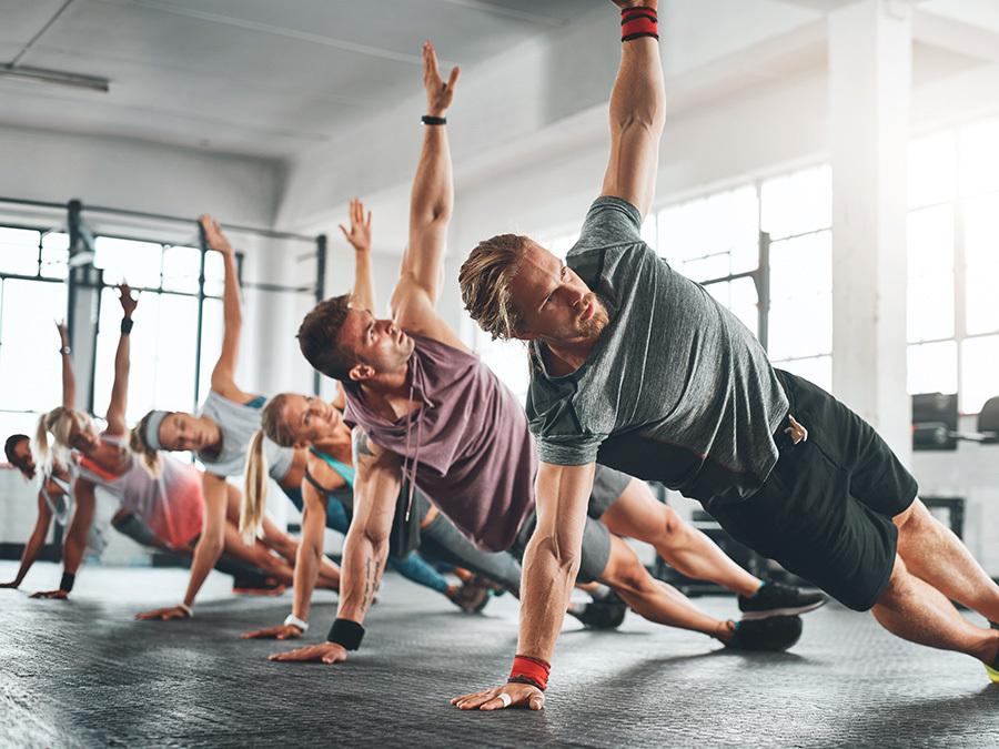 Gruppe von Sportlern in seitlichen Plank-Übungen in einem lichtdurchfluteten Fitnessstudio.
