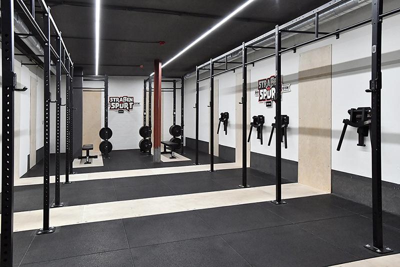 Modernes Fitnessstudio mit Kreuzhebe-Stangen, Hanteln und freier Trainingsfläche in strukturiertem Schwarz und Weiß.